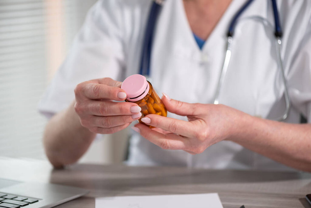 Женщина-врач смотрит на бутылку таблеток в медицинском кабинете - Фото, изображение