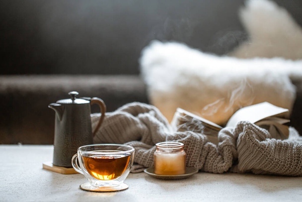 Copa de vidrio de té, tetera, vela con elemento de punto. El concepto de confort y calidez en el hogar. - Foto, imagen