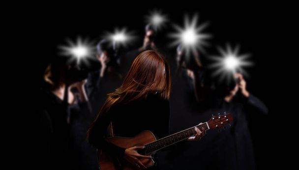 Niezidentyfikowana kobieta długie brązowe czarne włosy grać na gitarze i śpiewać piosenkę nad fotografem i reporterem wiadomości jako supergwiazda, piosenkarz ludzie noszą czarny materiał, przestrzeń kopiowania - Zdjęcie, obraz