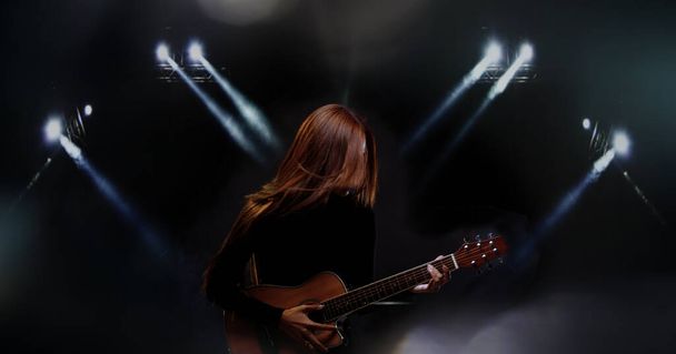 Bella donna asiatica lunghi capelli marroni neri suonare la chitarra e cantare una canzone sul palco con fumo di illuminazione, persona non identificata indossare un panno nero, spazio copia - Foto, immagini