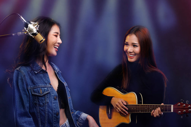 Dwie piękne azjatyckie piosenkarki Kobiety śpiewać piosenkę i grać na gitarze na scenie kawiarni, miłośnicy Lgbt wyrazić uczucie miłości podczas sesji koncertowej, uśmiech i spojrzeć na siebie - Zdjęcie, obraz