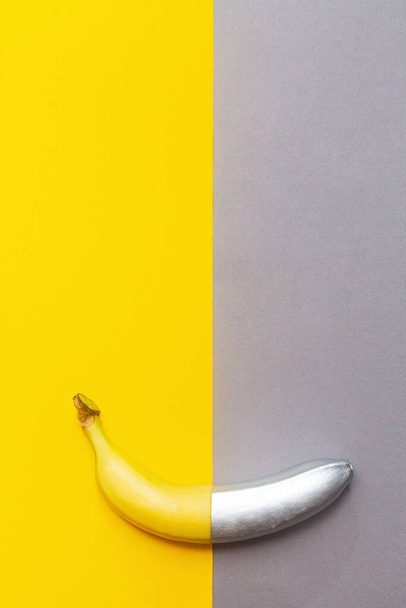 Malowany srebrny banan na żółto-szarym tle. Minimalistyczny abstrakcyjny obraz żywności - Zdjęcie, obraz