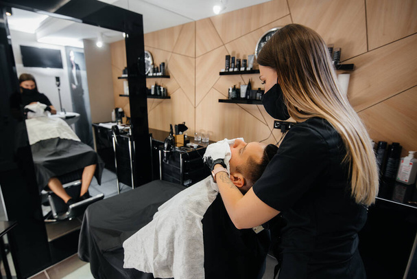 A professional stylist in a modern stylish barbershop shaves and cuts a young man's hair. Beauty salon, hair salon - Fotoğraf, Görsel
