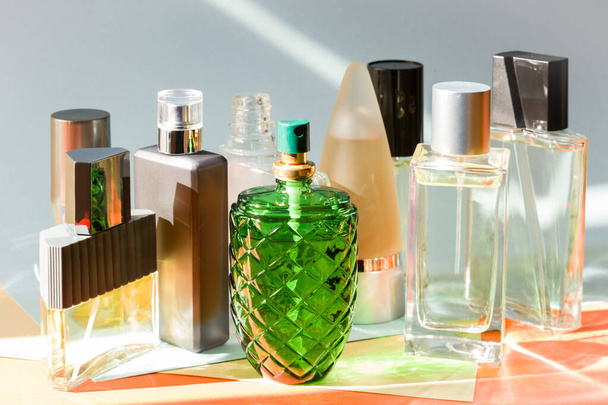 Verschillende parfumflesjes zijn gegroepeerd tegen een veelkleurige achtergrond met zachte tinten, de zonnestraal zorgt voor een aangenaam effect. - Foto, afbeelding