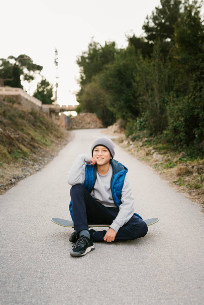 Portrait Of A Teen Boy sitting on his skateboard in a path - Фото, изображение