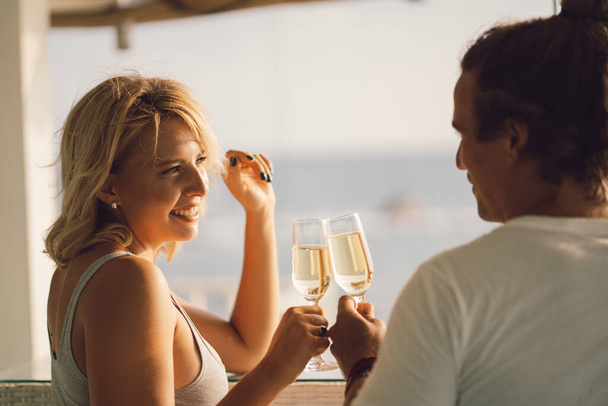 Glückliches Paar trinkt Wein am Strand. Verliebtes Paar vor dem Hintergrund des Sonnenuntergangs. Valentinstag im Urlaub. Reise, Liebe, Jugend-Lifestyle-Konzept.  - Foto, Bild