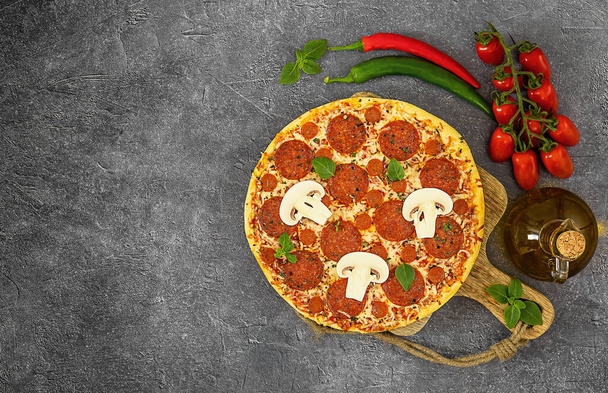 Sabrosa pizza de pepperoni e ingredientes de cocina tomates, chile, albahaca sobre fondo gris. Vista superior, espacio de copia. - Foto, imagen