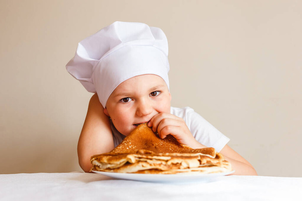 Seven-year-old boy in chef's cap eats pancakes at carnival - Zdjęcie, obraz