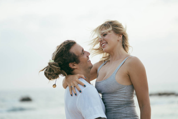 Schöne Paar tanzen lächelnd umarmt auf dem Strand Hintergrund. Valentinstag im Urlaub. Paar am Strand. Ein Mann hält ein Mädchen auf dem Arm. - Foto, Bild