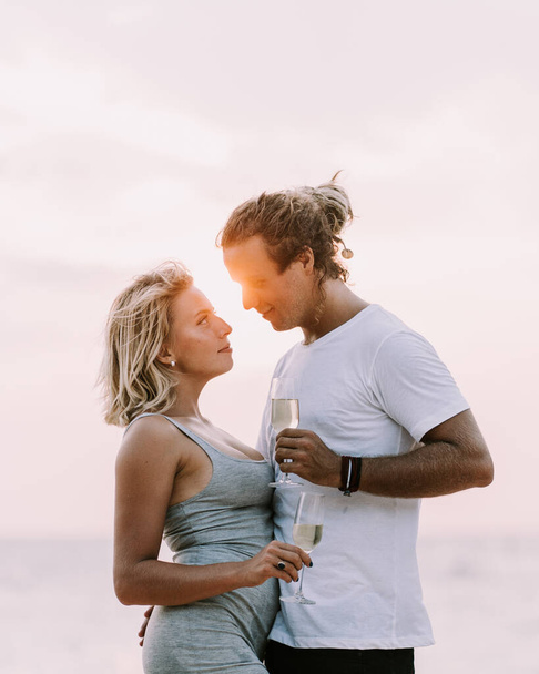 Happy couple drink wine on the beach. Couple in love on sunset background. Valentines day in vacation. Travel, love, youth lifestyle concept. Look into the eyes close up view couple drinking vine on sunset - Fotografie, Obrázek