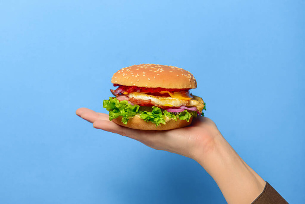 Homemade beef grilled hamburger in a hand over bright blue background. Copy space banner. Junk food, fast food concept. - Foto, Bild