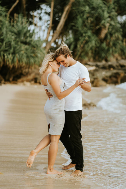 Beautiful couple dancing smiling embracing on the beach background. Valentines day on vacation. Couple on the beach. A man holds a girl in his arms. - 写真・画像