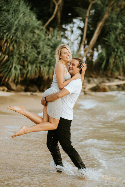 美しいカップルのビーチの背景に抱擁笑みを浮かべて踊る。休暇中のバレンタインデー。ビーチでカップル。男は腕の中に女の子を持っている. - 写真・画像