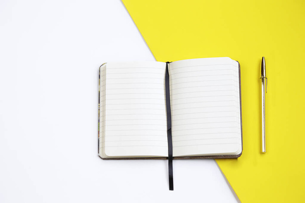 Draufsicht auf ein offenes Notizbuch mit goldenem Stift vor weißem und gelbem Hintergrund - Foto, Bild