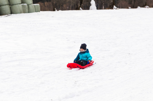 Un niño con trineo rojo en la nieve - Foto, imagen