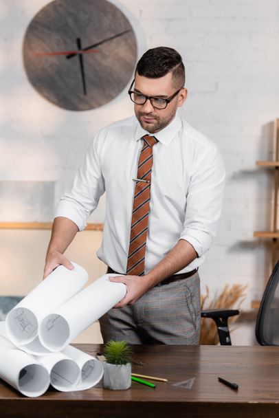 architect in eyeglasses holding blueprint while standing at workplace - Фото, зображення