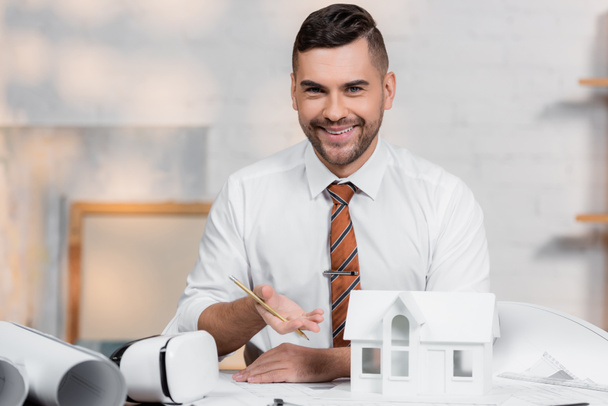 happy architect looking at camera while pointing at house model - Photo, Image