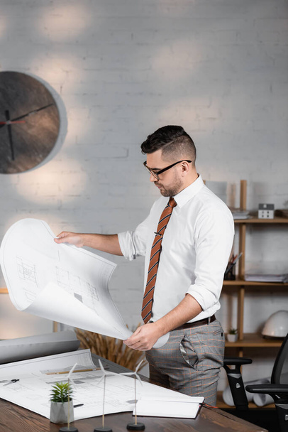 architect holding blueprint near models of wind turbines on desk - Foto, Bild
