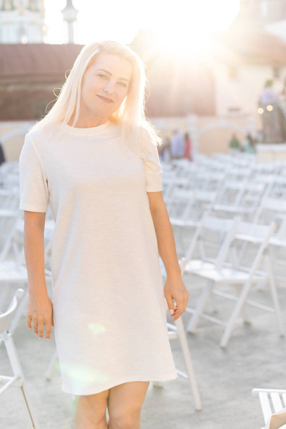 vonzó nő öltözött fehér ruha nyáron szabadtéri színház széken egyedül, tavaszi utcai divat trend, társadalmi távolság - Fotó, kép