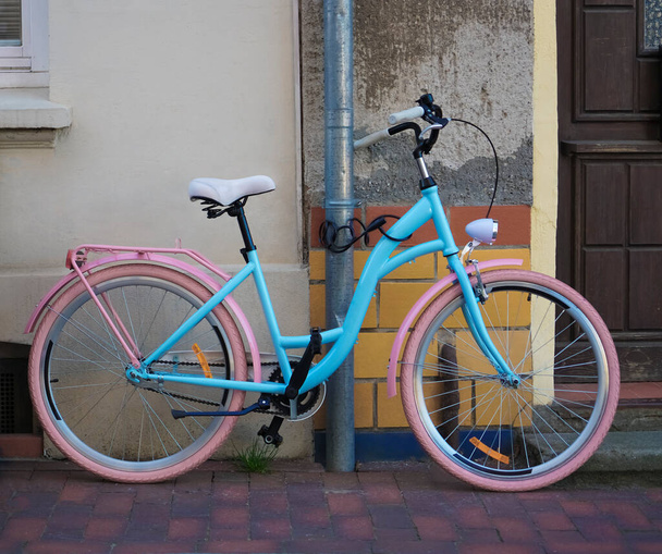 nueva bicicleta de época y pared de azulejos decorativos en Wismar, Alemania. bicicleta rosa y azul de pie cerca de la puerta de madera. - Foto, imagen