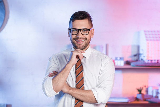 happy architect in eyeglasses looking at camera while standing in office - Zdjęcie, obraz
