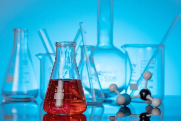 A glass flask with red liquid and a molecule structure on a lab table - Fotoğraf, Görsel