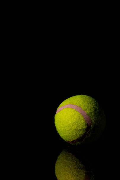 A vertical shot of a green tennis ball isolated on a dark background - Foto, afbeelding