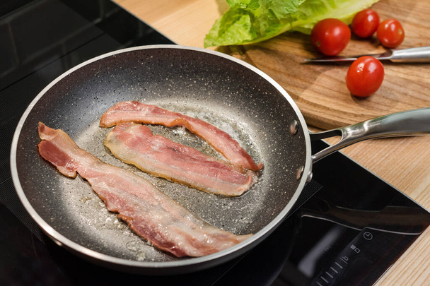 Slices of fresh fried bacon in a pan for breakfast, ingredients for chicken caesar salad, cooking on real kitchen, top view - Фото, изображение
