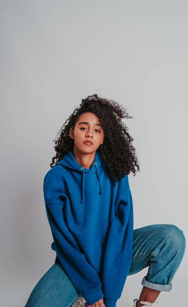 A beautiful curly-haired girl posing in a blue sweater and jeans on a white background - 写真・画像