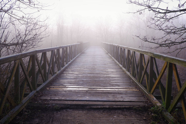 A beautiful view of an old wooden bridge in a misty weather - Фото, изображение