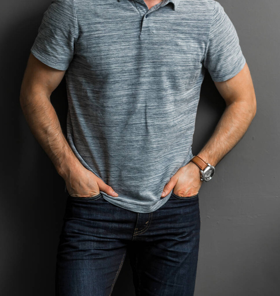 Μια άποψη ενός άνδρα που φοράει ένα γκρι μπλουζάκι πόλο ακουμπισμένο σε έναν γκρίζο τοίχο - Φωτογραφία, εικόνα
