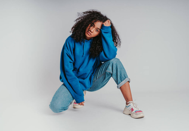 A beautiful curly-haired girl posing in a blue sweater and jeans on a white background - Фото, изображение