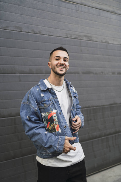 A vertical shot of a young trendy male in streetwear posing and smiling - Φωτογραφία, εικόνα