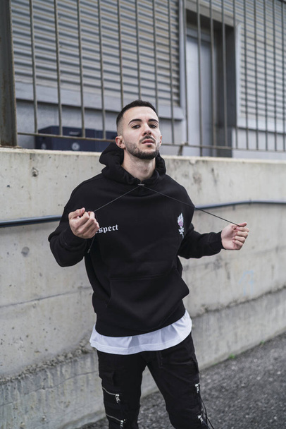 A vertical shot of a young trendy male posing in a black streetwear outfit - Zdjęcie, obraz