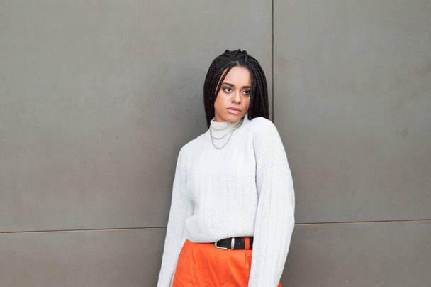 An attractive Afro-American woman with dreads wearing bright orange pants and a sweater - Zdjęcie, obraz
