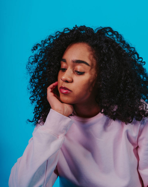 A portrait of a young Hispanic female with curly hair sitting against a blue background - Фото, зображення