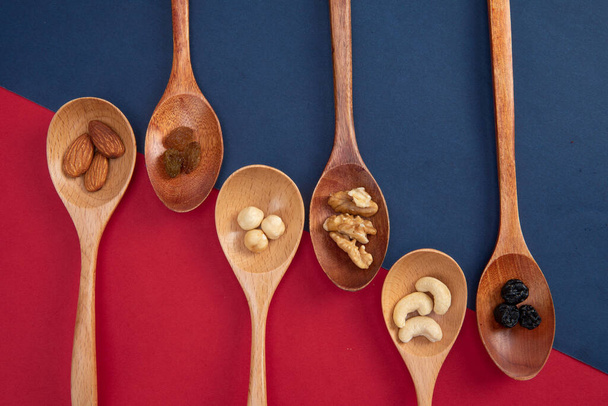 A top view of nuts and raisins assortment in wooden spoons isolated on red-blue background - Foto, Imagen