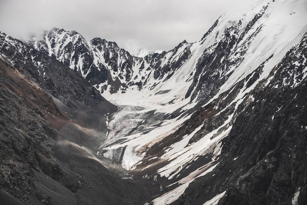 Атмосферный минималистский альпийский ландшафт большой снежной горы с массивным ледником. Облачное небо над большими скалистыми горами. Язык ледника рядом со склоном горы, покрытым снегом. Величественные пейзажи на большой высоте - Фото, изображение
