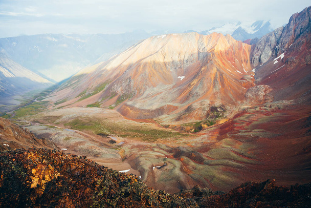Ζωντανό πολύχρωμο τοπίο της καταπράσινης κοιλάδας ανάμεσα σε μεγάλα βραχώδη βουνά. Όμορφο ορεινό τοπίο της γιγαντιαίας βουνοκορφής. Πράσινα κόκκινα πορτοκαλί κίτρινα βράχια και πέτρες στην κοιλάδα. Πολύχρωμοι τεράστιοι βράχοι. - Φωτογραφία, εικόνα