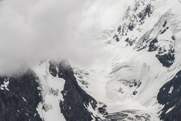 Atmospheric minimalist textured alpine landscape with massive glacier on big mountain in low clouds. Background of snowbound mountainside. Cracks on ice. Majestic foggy misty scenery on high altitude. - Photo, Image