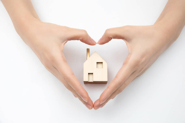 A top view of hands forming a heart over a small wooden house-real estate concept - Photo, Image