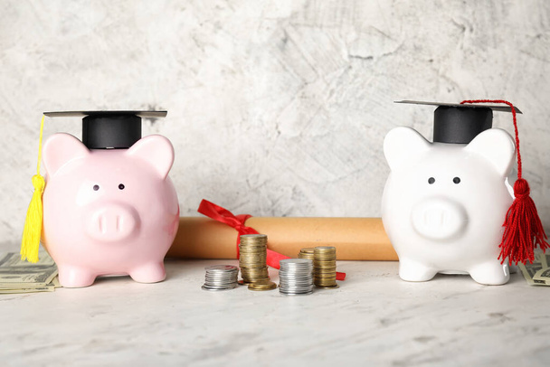Piggy τράπεζες με καπέλα αποφοίτησης, τα χρήματα και το δίπλωμα σε ελαφρύ φόντο - Φωτογραφία, εικόνα