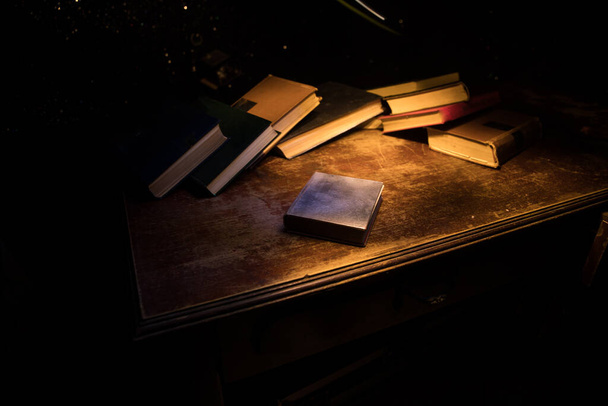 Bir yığın eski kitap. Ahşap masanın üzerinde antika bir kitap. Karanlıkta parlayan bir kitabın etrafında sihirli bir yıldırım. Seçici odak - Fotoğraf, Görsel