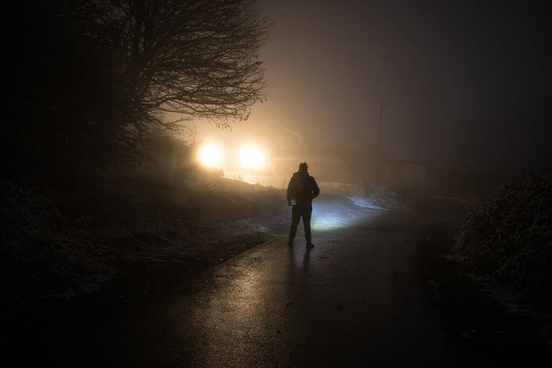 Egy ember sziluettje áll a sötét erdőben a fénnyel. Horror halloween koncepció. furcsa sziluett egy sötét kísérteties faluban - Fotó, kép