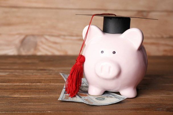 Hucha con sombrero de graduación y billetes de dólar sobre fondo de madera - Foto, Imagen