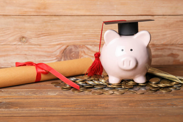 Hucha con sombrero de graduación, diploma y monedas sobre fondo de madera - Foto, Imagen