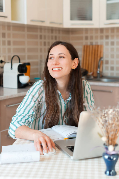 Muotokuva hymyilevä nuori nainen ja katselee pois, kun istuu pöydän ääressä keittiössä - Valokuva, kuva