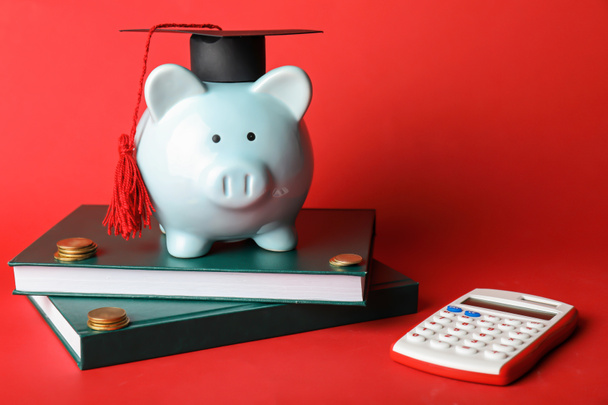 Piggy bank with graduation hat, books, calculator and coins on color background - Photo, Image