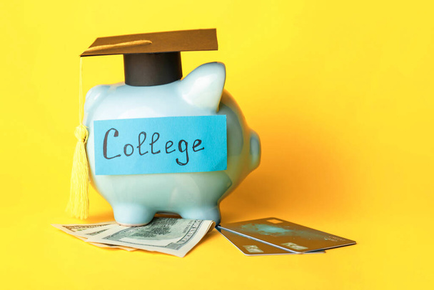 Hucha con sombrero de graduación, tarjetas de crédito y billetes de dólar sobre fondo de color - Foto, imagen