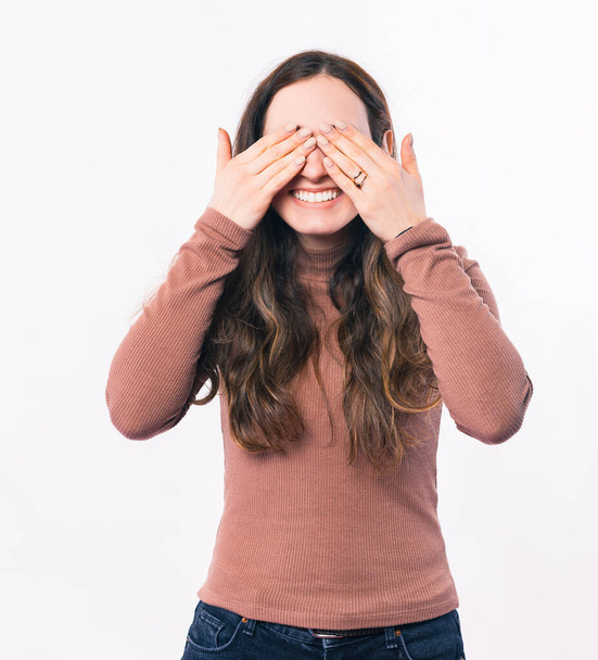 Πορτρέτο μιας χαμογελαστής νεαρής γυναίκας που καλύπτει τα μάτια της με τα χέρια της. - Φωτογραφία, εικόνα